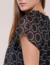 Blusa holgada de gasa negra con estampado geométrico de círculos blancos, cuello redondo fruncido con volados y mangas cortas de corte mariposa.