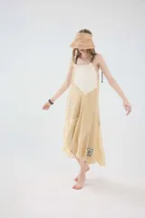 Vestido midi de lino color beige, con diseño de cortes irregulares, tirantes dobles finos y ruedo asimétrico.