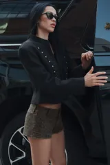 Blazer negro de corte entallado y manga larga con hombreras, cuello redondo y cierre frontal con gancho metálico. Presenta detalles de pasamanería bordada a tono y botones dorados en el delantero.