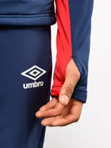 Buzo de entrenamiento Umbro del Club Nacional de Football, con cierre frontal parcial y cuello alto. Presenta un diseño con bloques de color azul, blanco y rojo, con panel frontal acolchado y mangas largas con aberturas para pulgares.
