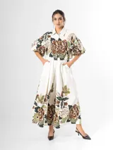 Conjunto de dos piezas confeccionado en viscosa con estampado floral en tonos marrones y verdes sobre base blanca. Incluye una blusa tipo camisa corta con cuello solapa, cierre frontal de botones y mangas abullonadas con diseño globo, y un pantalón tipo culotte de tiro alto, amplio y fluido con pinzas en la cintura.