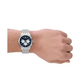 Reloj Emporio Armani modelo Antonio, con caja plateada de acero inoxidable de 41mm de diámetro, esfera azul con tres subesferas plateadas, agujas plateadas luminiscentes y calendario a las 6. Pulsera de acero inoxidable plateada con cierre desplegable. Resistente al agua hasta 50 metros.