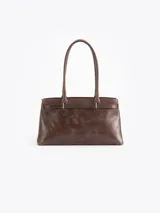Cartera tipo shopper de cuero vacuno marrón, con silueta estructurada, doble asa de hombro y herrajes metálicos plateados. Incluye tira decorativa con candado y llave colgantes.