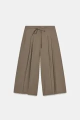 Pantalón culotte de tiro medio color marrón topo, con pliegues marcados en el delantero y cintura ajustable con cordones. Cierre frontal con cremallera y gancho metálico.