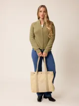 Bolso tipo tote de diseño acolchado con patrón de rombos, confeccionado en poliamida negra. Presenta un bolsillo frontal central de pana con el logo de la marca bordado en dorado, detalles de ribetes en pana negra y botones metálicos dorados en la parte superior. Incluye correas de hombro resistentes y forro interior de algodón a cuadros.