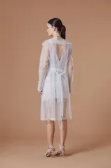 Trench ligero de tul color nude, con diseño abierto, solapas clásicas y mangas largas. Presenta una caída fluida y transparente, ideal para superposiciones elegantes.