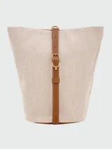 Cartera tipo bucket de tamaño pequeño, confeccionada en lona color crudo con detalles en cuero color tostado. Presenta una base redondeada, cierre de solapa con broche y correa ajustable para llevar al hombro.