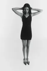 Vestido corto negro, ajustado al cuerpo, con breteles spaghetti finos y escote drapeado tipo cascada. Presenta frunces laterales que generan un efecto drapeado en la parte delantera.