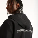 Campera New Balance Trackside de color negro, con capucha, cierre frontal completo y bolsillos laterales. Cuenta con el logo de la marca estampado en el pecho y detalles de líneas blancas en los laterales.