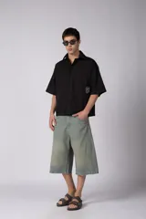 Camisa de manga corta negra 100% algodón, con calce boxy, cuello camisero, cierre frontal con botones y detalle de bordado blanco en la parte inferior.