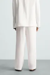 Pantalón de corte relajado confeccionado en tejido de lino. Presenta cintura elástica, bolsillos frontales, bolsillo trasero de vivo y cierre frontal con cremallera y botón.