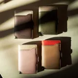 Billetera tarjetero automática con estructura de aluminio y revestimiento de cuero bicolor en tonos verde oliva y beige. Cuenta con un cierre de broche a presión y el logo de la marca grabado en la parte inferior.