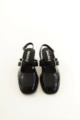Zapatos tipo Mary Jane de charol color negro, con taco bloque, talón descubierto y doble tira frontal con hebillas metálicas.