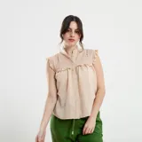 Camisa sin mangas color beige, con cuello alto con volados, detalles de encaje calado en los hombros y parte superior del pecho, y cierre frontal con botones.