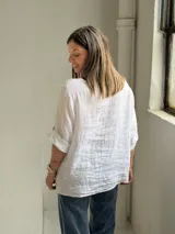 Blusa de lino color blanco, de corte amplio, con escote redondo y mangas tres cuartos con presillas para arremangar.
