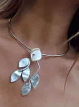 Gargantilla rígida plateada con dije central de piedra natural blanca y apliques de hojas plateadas.