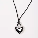 Collar con dije de corazón plateado colgando de cordón negro.
