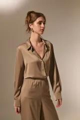 Camisa de poliéster con acabado satinado, de corte holgado, cuello camisero clásico, cierre frontal con botones y mangas largas con puños.