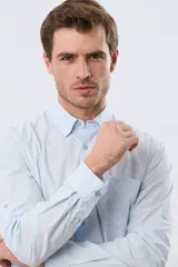 Camisa celeste de manga larga confeccionada en algodón, con cuello camisero, cierre frontal de botones, bolsillo en el pecho y diseño de cuadros sutiles.