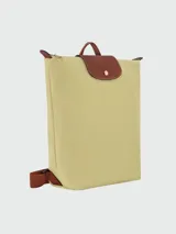 Mochila de diseño minimalista en color beige, con solapa y asa superior en cuero marrón texturizado. Cuenta con correas ajustables en color marrón y cierre principal.