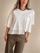 Remera oversize color blanco de manga corta, con costura central frontal y detalle de puntilla bordada en el ruedo inferior.