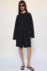 Bermuda de algodón color negro, con tiro medio, cintura elástica ajustable con cordones y bolsillos laterales ocultos en costura.