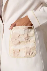 Blazer de lana soft color camel, con corte recto y solapas clásicas. Presenta detalles de encaje blanco en los puños y apliques de perlas en los bolsillos frontales.