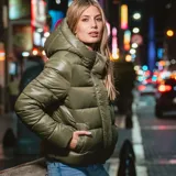Campera puffer verde con capucha y cuello alto. Tiene cierre frontal con cremallera y botones a presión. Cuenta con dos bolsillos externos y sistema de ajuste regulable en la parte baja. Es acolchada, liviana y de corte regular.