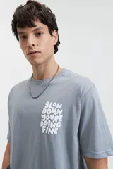 Remera celeste de manga corta con cuello redondo y estampado frontal con la frase "Slow Down You're Doing Fine" en letras blancas con efecto 3D.