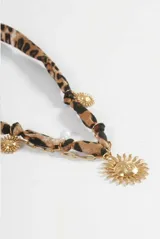 Collar con tira de tela estampada en animal print, adornado con un dije central grande en forma de sol y pequeños dijes de sol distribuidos a lo largo de la tira, todos en tono dorado.
