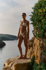 Conjunto de bikini color blanco hueso, confeccionado en lycra mate. El corpiño es con aro, tazas con frunces y breteles anchos regulables. La bombacha es vedetina con tiras ajustables en los laterales.