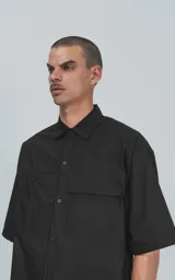Camisa de manga corta en popelina de algodón, con diseño oversize y cierre frontal de botones. Presenta dos bolsillos delanteros, uno con solapa y otro con ojal y botón.