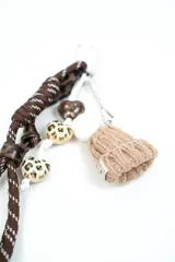 Llavero decorativo con mosquetón metálico, compuesto por tiras de cordón marrón con costuras blancas, tiras con estampado animal print tipo leopardo, colgantes en forma de corazón con motivos estampados y un dije en miniatura de gorro tejido de lana en color tostado con pompón blanco.