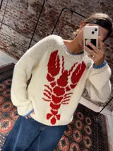 Buzo de lana merino color crema con diseño de langosta tejida en color rojo en el frente. Presenta cuello redondo, mangas largas con detalles en azul en los puños y un corte holgado.