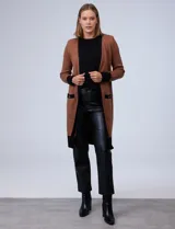 Cardigan largo tejido color marrón con ribetes negros en contraste, bolsillos delanteros y mangas largas.