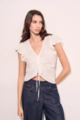 Blusa blanca de algodón con bordado broderie, escote en V con cordón ajustable, mangas cortas con volados y corte al cuerpo.