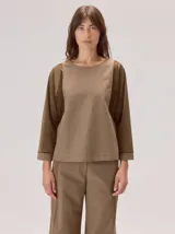Camisa de manga larga con diseño bicolor en tonos tierra. Presenta un panel frontal y trasero en color beige, contrastado con mangas de un tono marrón más oscuro y textura satinada. Posee cuello redondo y corte recto.