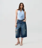 Bermuda jorts de jean azul oscuro con talle medio, corte amplio y roturas con desgastes localizados. Cuenta con bolsillos y cierre tradicional.