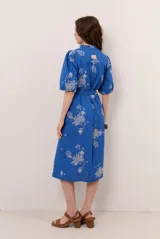 Vestido midi azul con estampado floral blanco, cuello en V, mangas cortas abullonadas y cierre frontal de botones. Incluye un lazo ajustable para la cintura.