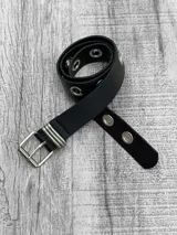 Cinto negro de cuero sintético con hebilla metálica plateada y ojalillos metálicos plateados.