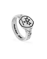 Anillo plateado con diseño de sello y dibujo de una cara con estrellas en los ojos.