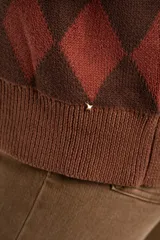 Cardigan de punto con diseño de rombos en tonos marrón y terracota, cuello en V, cierre frontal con botones y mangas largas con puños acanalados.