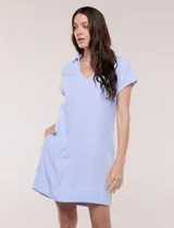 Vestido corto de lino color celeste con cuello camisero, escote en V, mangas cortas, bolsillos laterales invisibles y silueta holgada.