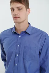 Camisa azul de manga larga con cuello clásico, cierre con botones y bolsillo en el pecho.