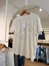 Remera blanca de algodón con cuello redondo, manga corta y calce recto, con un delicado estampado floral en trazo negro continuo.