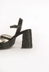 Sandalias de tacón alto y plataforma, color negro, con capellada de tiras cruzadas y cierre de hebilla en el tobillo. Cuentan con textura grabada en todo su diseño.