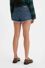 Short de denim de tiro bajo para mujer, confeccionado en algodón con baja elasticidad. Presenta un lavado azul medio con efecto desgastado, diseño de cinco bolsillos y dobladillo deshilachado con flecos.