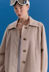 Trench midi color camel, confeccionado en mezcla de algodón y nylon. Presenta cuello clásico, cierre frontal con botones, tajos laterales y bolsillos internos. Es una prenda repelente al agua con diseño versátil y funcional.
