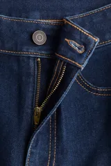 Jean de denim oscuro con ligero estiramiento, tiro alto, cierre de botón y piernas amplias con bajos acampanados. Presenta bolsillos decorativos delanteros y bolsillos traseros.