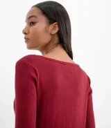 Suéter de punto color rosado, con cuello barco, mangas largas y puños con botones decorativos. El dobladillo también es acanalado.